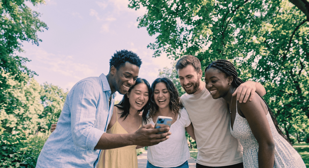 Social Media Management Freelancer: Fünf junge Menschen lachen ein Smartphone an